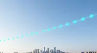 A glowing ribbon of turquoise light points arcing across a bright blue morning sky above a modern city skyline