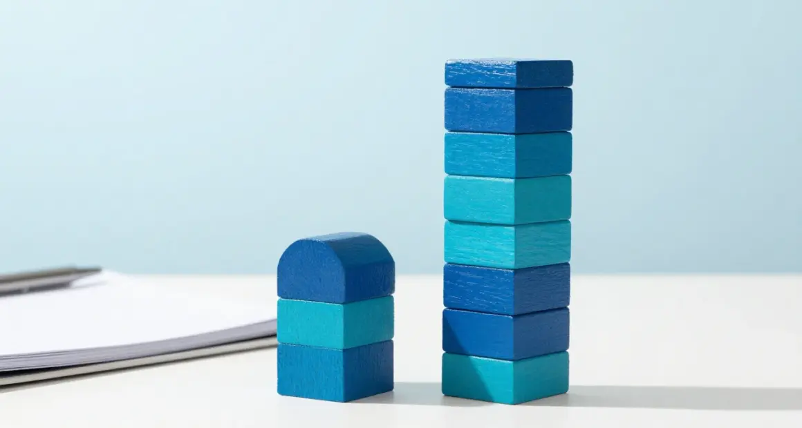 Two towers of cobalt and turquoise wooden blocks on a white desk, the right tower much taller than the left, a notebook and pen beside them