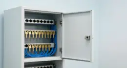 An open white key cabinet with rows of brass keys mounted beside a rack of network switches with blue cables