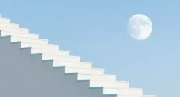 A steep white staircase of server blades rising toward a pale full moon in a bright blue daytime sky