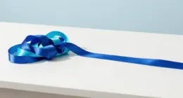 A tangled knot of cobalt and turquoise ribbon on a white desk, with the same ribbon running out into one smooth straight line
