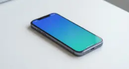 A smartphone lying on a bright white desk, its blank screen glowing in blue and turquoise