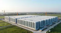 Aerial view of a large data center campus under construction with rows of long white halls and tower cranes in green fields